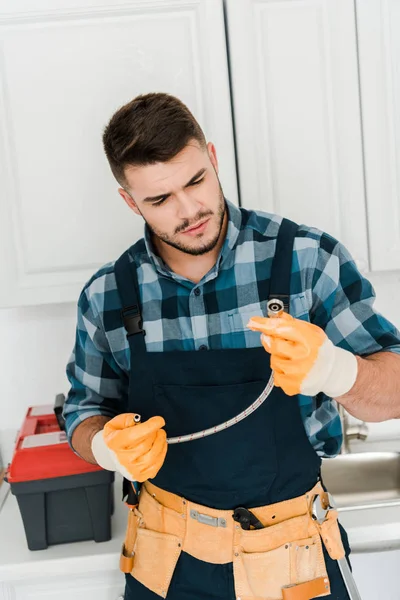 Bonito reparador em luvas de borracha olhando para mangueira de metal — Fotografia de Stock