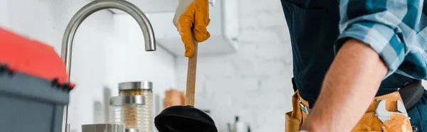 Panoramic shot of handyman holding plunger in kitchen — Stock Photo