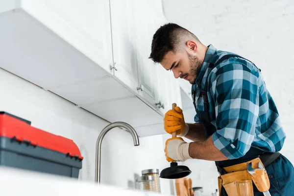 Foco seletivo do reparador segurando êmbolo na cozinha — Fotografia de Stock