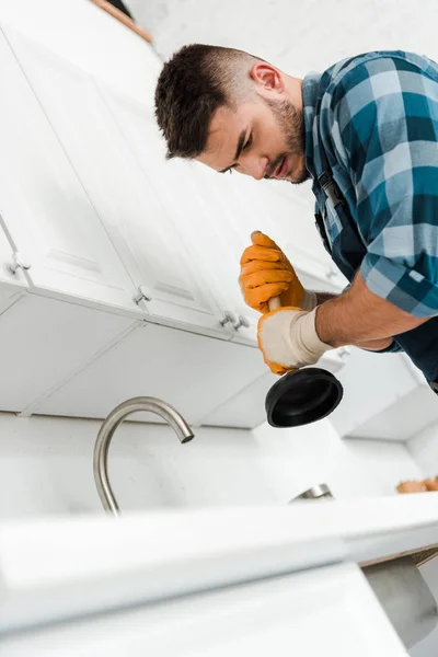 Low angle view of repairman holding plunger in kitchen — Stock Photo