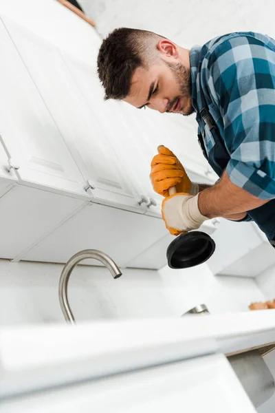 Vista de ángulo bajo del reparador sosteniendo el émbolo en la cocina - foto de stock