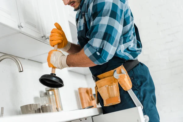 Vista recortada del manitas con el cinturón de herramientas que sostiene el émbolo en la cocina - foto de stock
