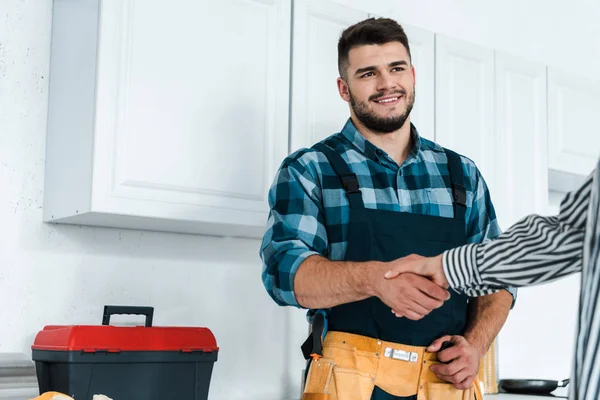 Cropped view of woman shaking hands with happy bearded handyman — Stock Photo