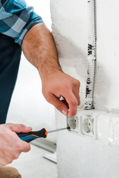 Vista cortada de handyman segurando chave de fenda perto de tomada de energia — Fotografia de Stock