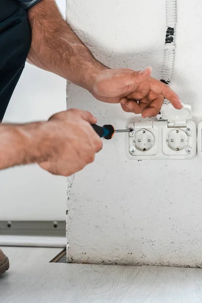 Cropped view of technician holding screwdriver near power socket — Stock Photo