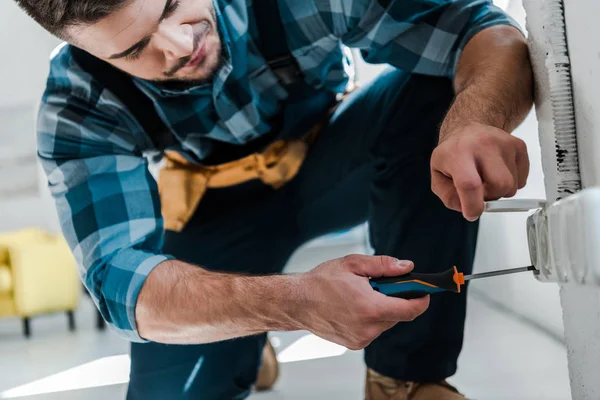 Bärtiger Reparateur in Uniform sitzt während er Steckdose mit Schraubenzieher fixiert — Stockfoto