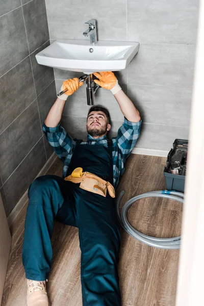 Reparador guapo que fija daño del agua con la llave ajustable en cuarto de baño - foto de stock
