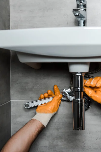 Ausgeschnittene Ansicht eines Reparateurs in Gummihandschuhen, der Wasserschäden mit verstellbarem Schraubenschlüssel behebt — Stockfoto