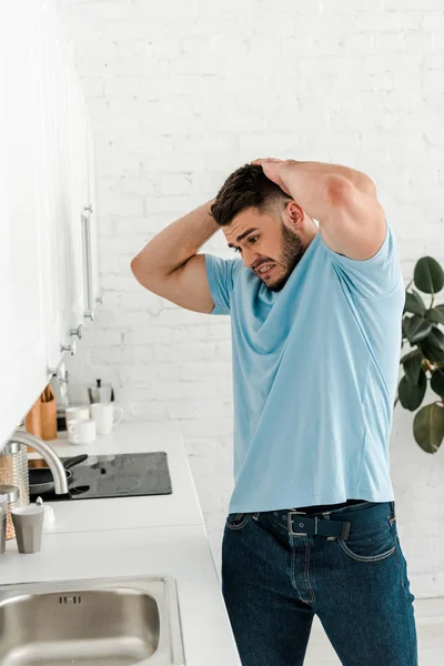 Aufgebrachter Mann berührt Kopf beim Blick auf Spüle in moderner Küche — Stockfoto