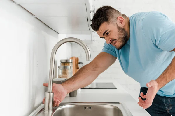 Homem zangado gesticulando perto da torneira na cozinha — Fotografia de Stock