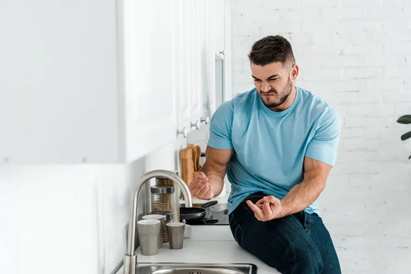 Messa a fuoco selettiva dell'uomo emotivo che mostra le dita medie e guarda il rubinetto in cucina — Foto stock