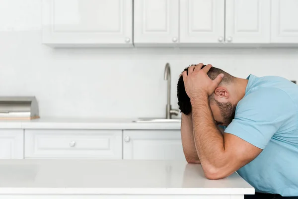 Homme frustré toucher la tête tout en étant assis près de la table dans la cuisine — Photo de stock