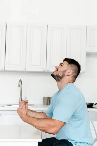 Side view of angry man screaming while sitting near table in kitchen — Stock Photo