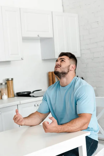 Homem irritado gesticulando enquanto sentado perto da mesa na cozinha — Fotografia de Stock