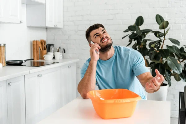 Wütender bärtiger Mann spricht auf Smartphone in der Nähe von Plastik-Waschschüssel — Stockfoto