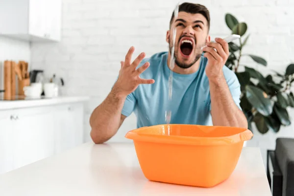 Foco seletivo de homem barbudo gritando enquanto olha para a água derramando em tigela de lavagem de plástico — Fotografia de Stock