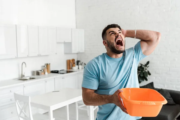 Screaming man holding plastic wash bowl near pouring water — Stock Photo