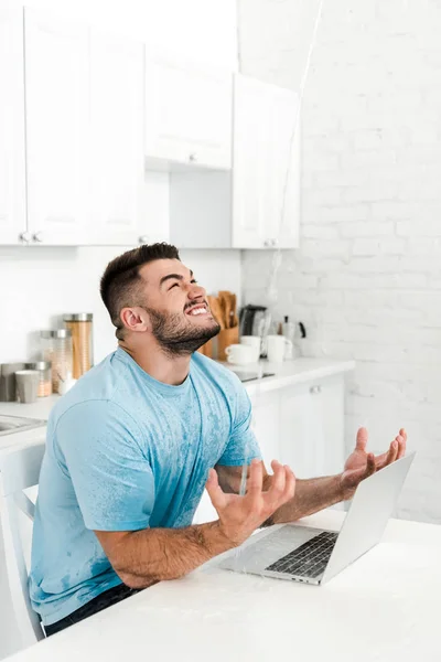 Messa a fuoco selettiva dell'uomo emotivo gesticolare mentre guarda l'acqua versare sul computer portatile in cucina — Foto stock