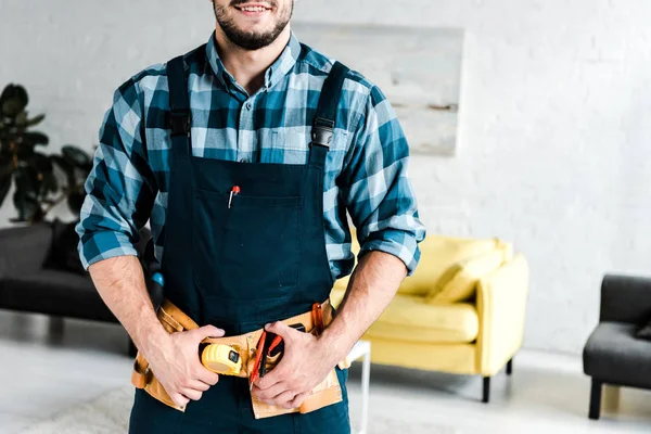 Ausgeschnittene Ansicht eines glücklichen Arbeiters, der Werkzeuggürtel im Wohnzimmer berührt — Stockfoto