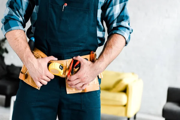 Ausgeschnittene Ansicht eines Arbeiters, der Werkzeuggürtel im Wohnzimmer berührt — Stockfoto