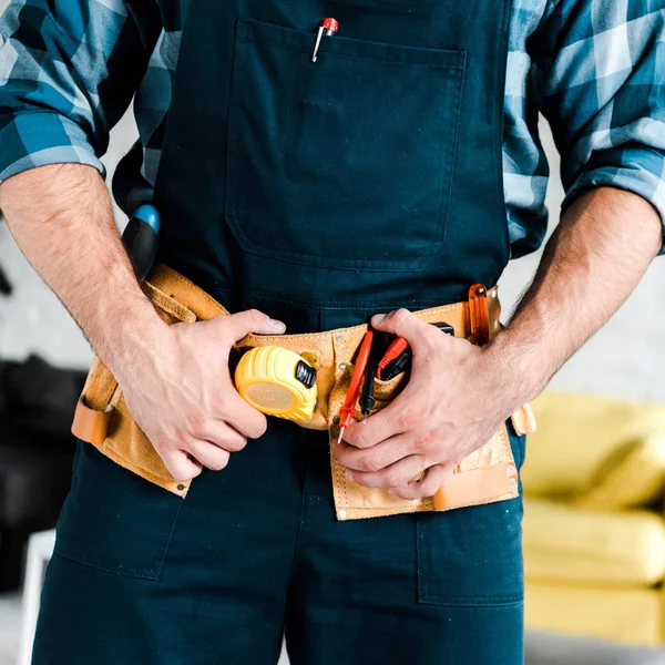 Ausgeschnittene Ansicht eines Heimwerkers, der Werkzeuggürtel im Wohnzimmer berührt — Stockfoto