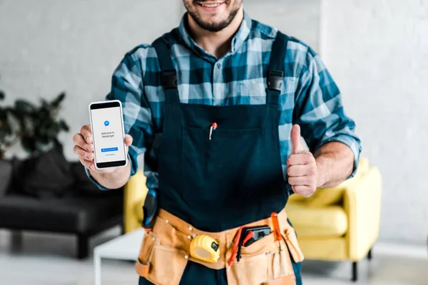 KYIV, UCRANIA - 31 de julio de 2019: vista recortada del hombre feliz sosteniendo el teléfono inteligente con la aplicación de mensajero en la pantalla y mostrando el pulgar hacia arriba — Stock Photo