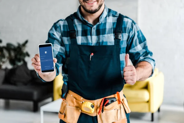 KYIV, UKRAINE - JULY 31, 2019: cropped view of happy man holding smartphone with facebook app on screen and showing thumb up — Stock Photo