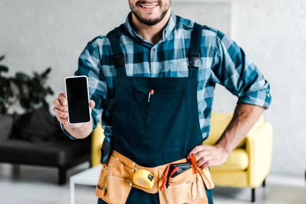 Cropped view of bearded man holding smartphone with blank screen and standing with hand on hip — Stock Photo