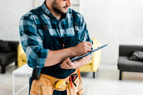 Abgeschnittene Ansicht eines bärtigen Arbeiters, der schreibt, während er Klemmbrett hält — Stockfoto