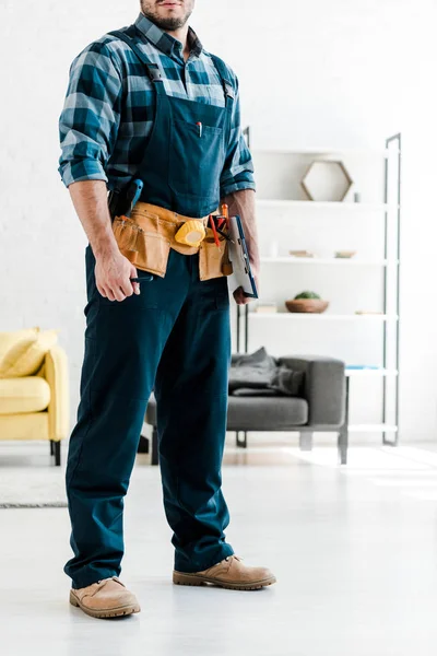 Vista ritagliata del lavoratore barbuto in casco di sicurezza che tiene appunti in soggiorno — Foto stock