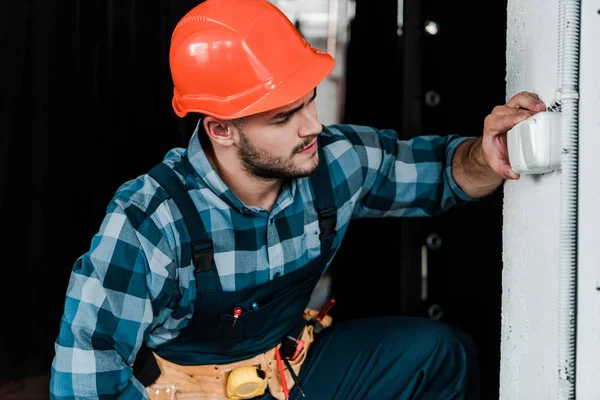 Bearded worker in safety helmet touching light switch — Stock Photo