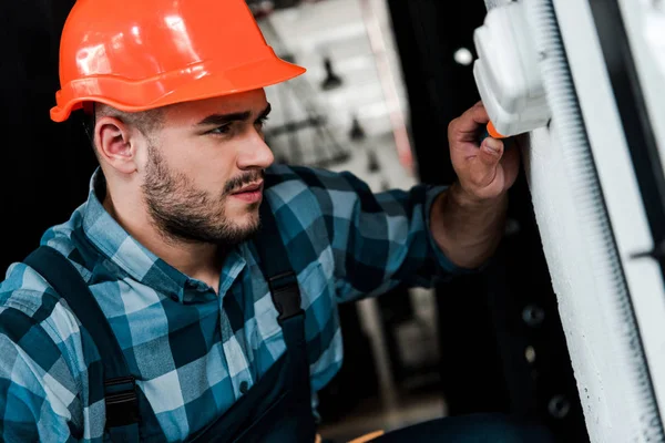 Trabajador guapo en casco de seguridad interruptor de luz táctil - foto de stock