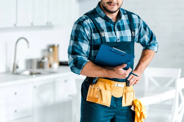 Обрезанный вид бородатого рабочего, стоящего с рукой на бедре и держащего планшет — стоковое фото