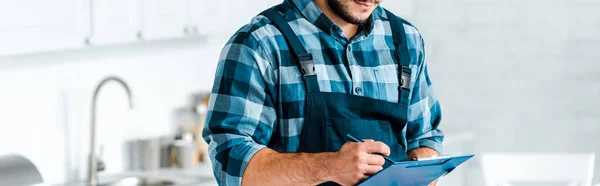 Panoramic shot of bearded workman holding clipboard and pen — Stock Photo