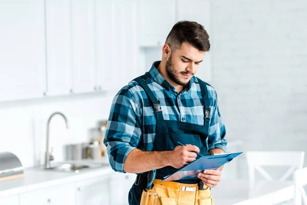 Красивый бородатый рабочий пишет, держа планшет на кухне — стоковое фото