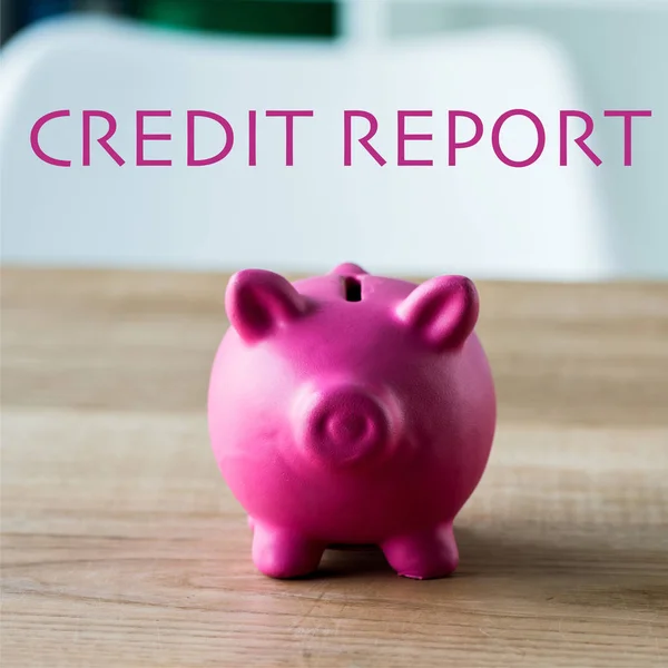 Pink piggy bank on wooden desk near credit report lettering in office — Stock Photo