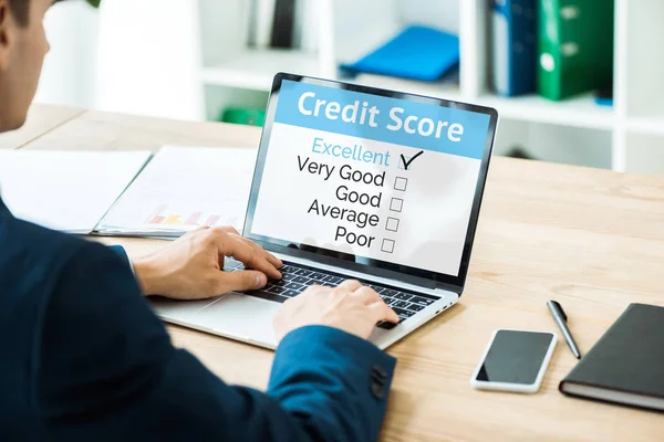 Selective focus of man typing on laptop with credit score lettering near smartphone with blank screen on table — Stock Photo