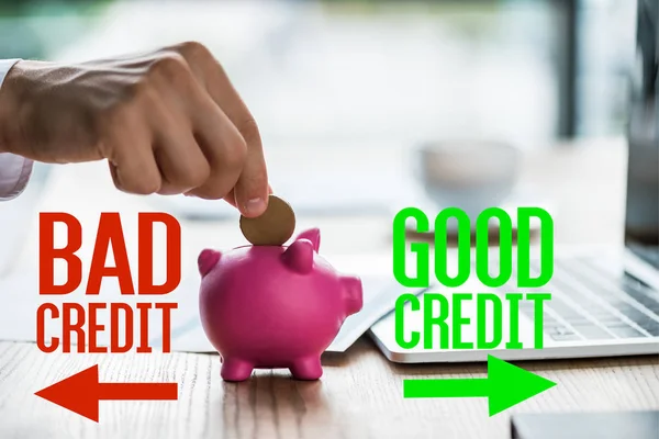 Abgeschnittene Ansicht von Geschäftsmann, der Münze in rosa Sparschwein in der Nähe schlechter Kreditwürdigkeit, guter Kreditbeschriftung und Laptop steckt — Stockfoto