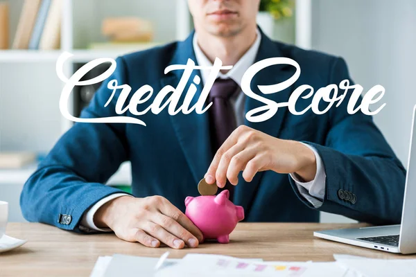 Vista recortada de hombre de negocios poner moneda metálica en alcancía rosa cerca de letras de puntuación de crédito - foto de stock