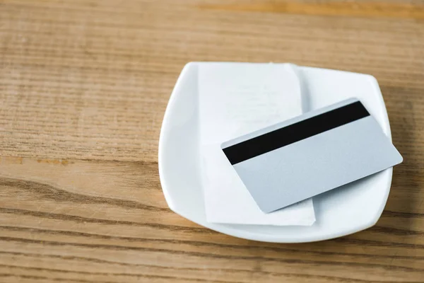 Carta di credito su placca bianca con ricevuta su tavolo in legno — Foto stock