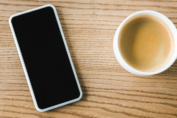 Вид сверху на смартфон с пустым экраном возле чашки кофе — стоковое фото