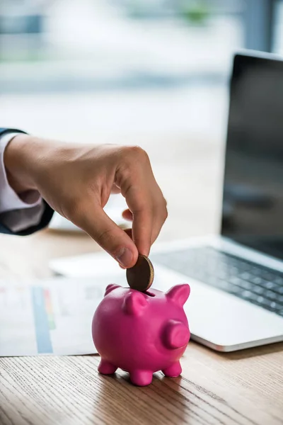 Cropped view of businessman putting coin into piggy bank near laptop — Stock Photo