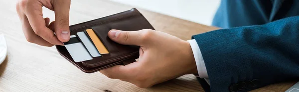 Plano panorámico del hombre de negocios tocando la tarjeta de crédito mientras sostiene la cartera negra - foto de stock