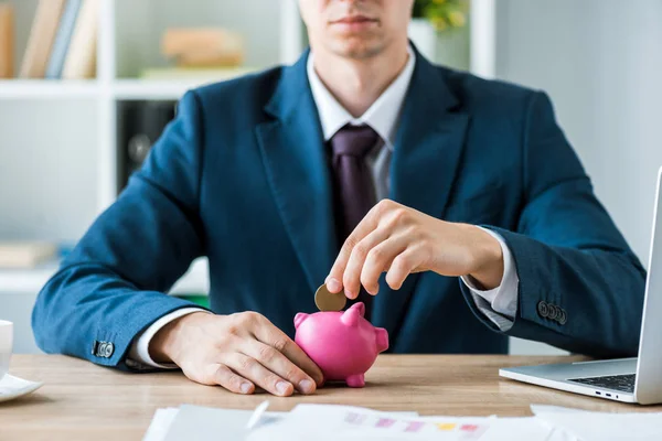 Cropped view of businessman putting metallic coin into pink piggy bank — Stock Photo