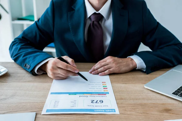 Cropped view of businessman holding pen near document with lettering and laptop on table — Stock Photo