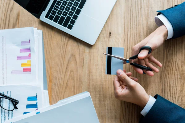 Top view of man cutting credit card with scissors near laptop — Stock Photo