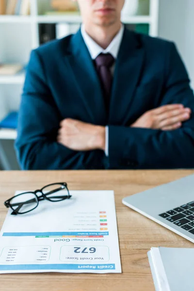 Foyer sélectif du document avec rapport de crédit près de l'ordinateur portable et l'homme avec les bras croisés — Stock Photo