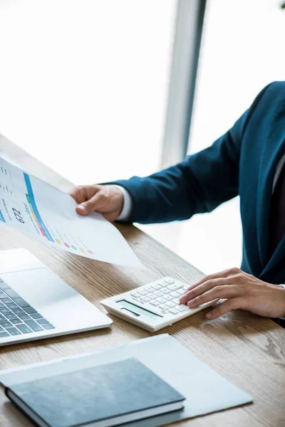 Cropped view of man holding paper with lettering and counting on calculator — Stock Photo