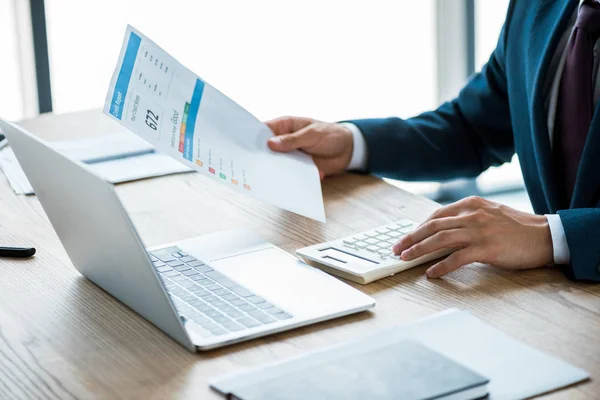 Cropped view of businessman holding paper with credit report lettering and counting on calculator — Stock Photo