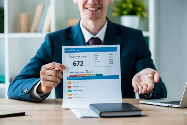 Enfoque selectivo de hombre alegre celebración de documento con letras de informe de crédito cerca de la computadora portátil en la oficina - foto de stock